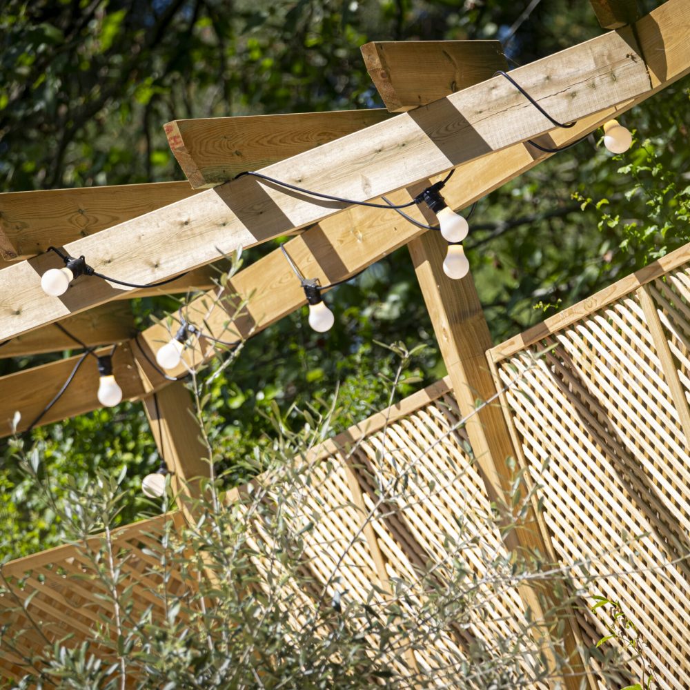 Timber garden pergola with decorative lighting and contemporary wooden trellis fencing in a professionally landscaped garden
