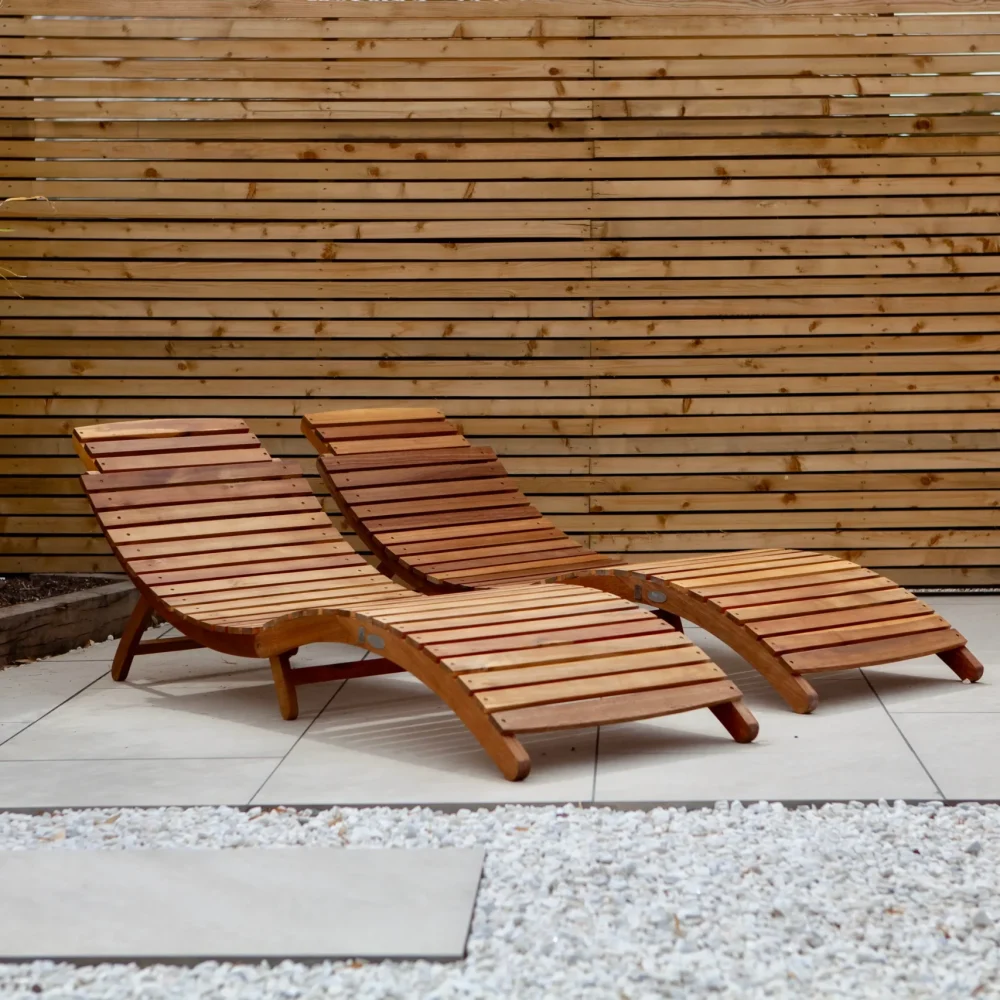 Modern garden patio with timber slatted fencing and wooden sun loungers by Bamboo Landscapes